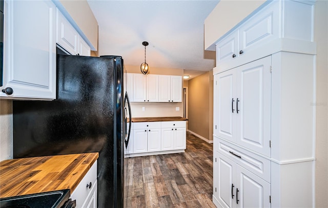 kitchen with pendant lighting, dark wood-type flooring, white cabinets, black fridge, and butcher block countertops