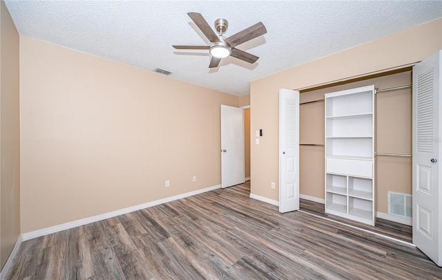 unfurnished bedroom featuring ceiling fan, a closet, dark wood-type flooring, and a textured ceiling