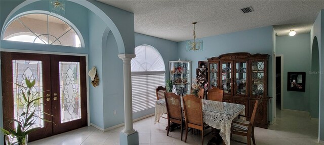 tiled dining room with ornate columns, french doors, a chandelier, and a textured ceiling