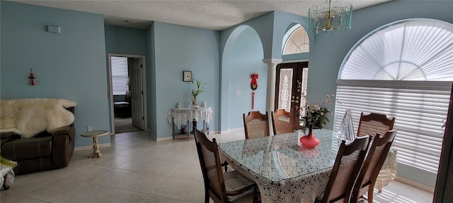 tiled dining area featuring an inviting chandelier, a textured ceiling, and ornate columns