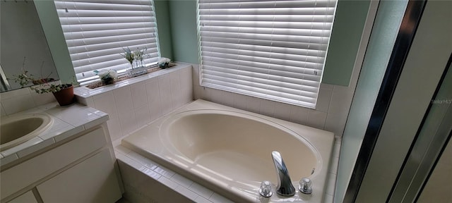 bathroom with tiled tub, vanity, and a healthy amount of sunlight