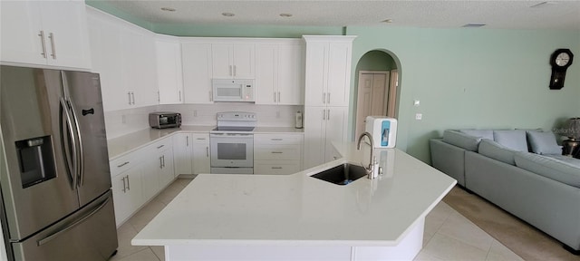 kitchen featuring white appliances, white cabinets, a center island with sink, and sink