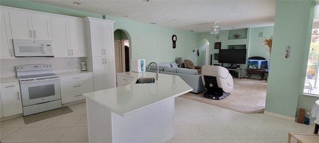 kitchen with tasteful backsplash, white cabinetry, an island with sink, sink, and white appliances