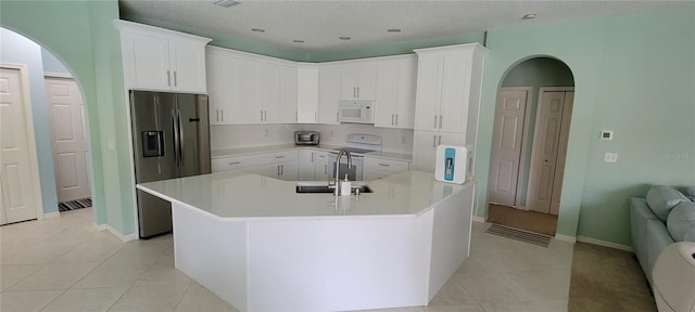 kitchen with sink, white cabinetry, light tile patterned floors, an island with sink, and white appliances