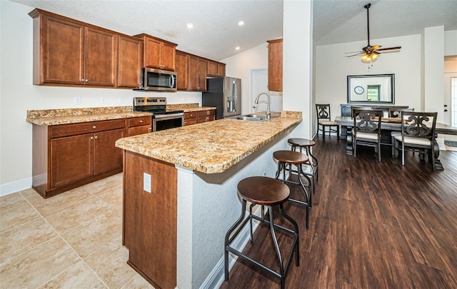 kitchen with lofted ceiling, kitchen peninsula, appliances with stainless steel finishes, a breakfast bar, and light hardwood / wood-style floors