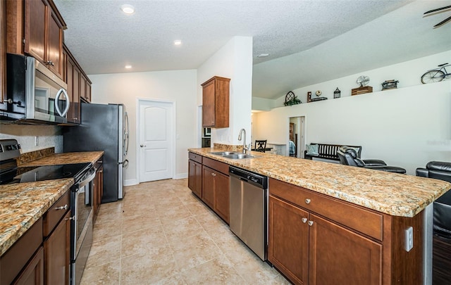 kitchen with sink, lofted ceiling, light stone countertops, appliances with stainless steel finishes, and a textured ceiling