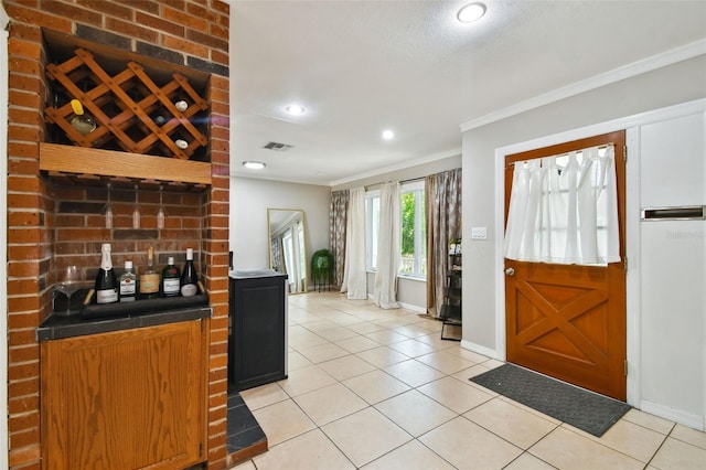 foyer entrance featuring ornamental molding, light tile patterned flooring, bar, and a textured ceiling