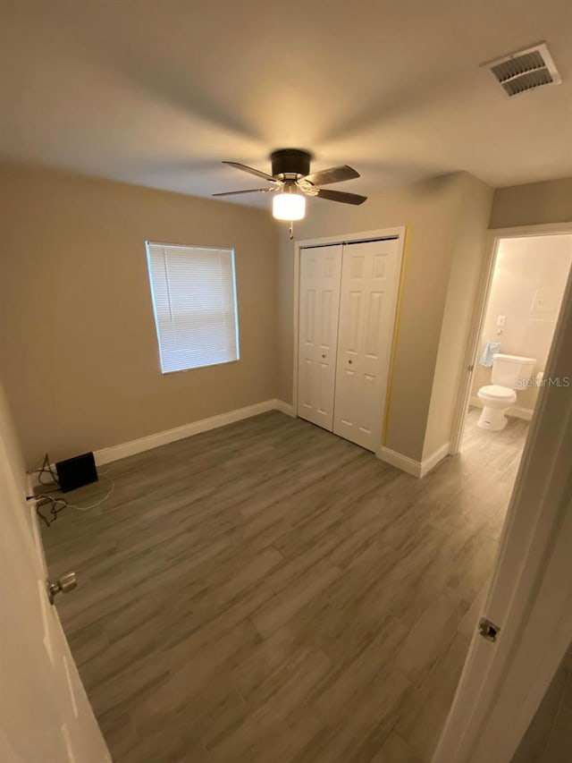 unfurnished bedroom with dark wood-type flooring, a closet, ensuite bath, and ceiling fan