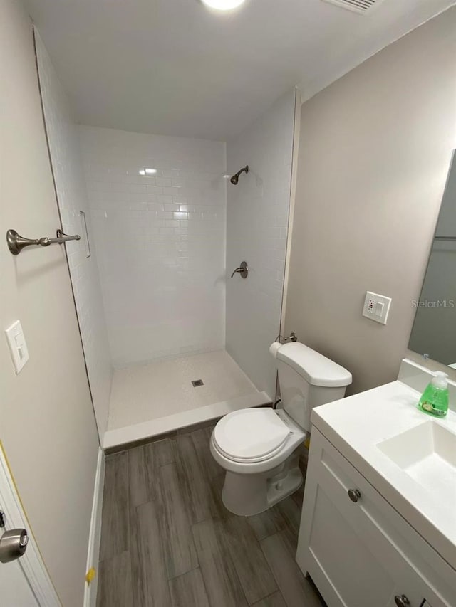 bathroom with hardwood / wood-style flooring, a tile shower, toilet, and vanity