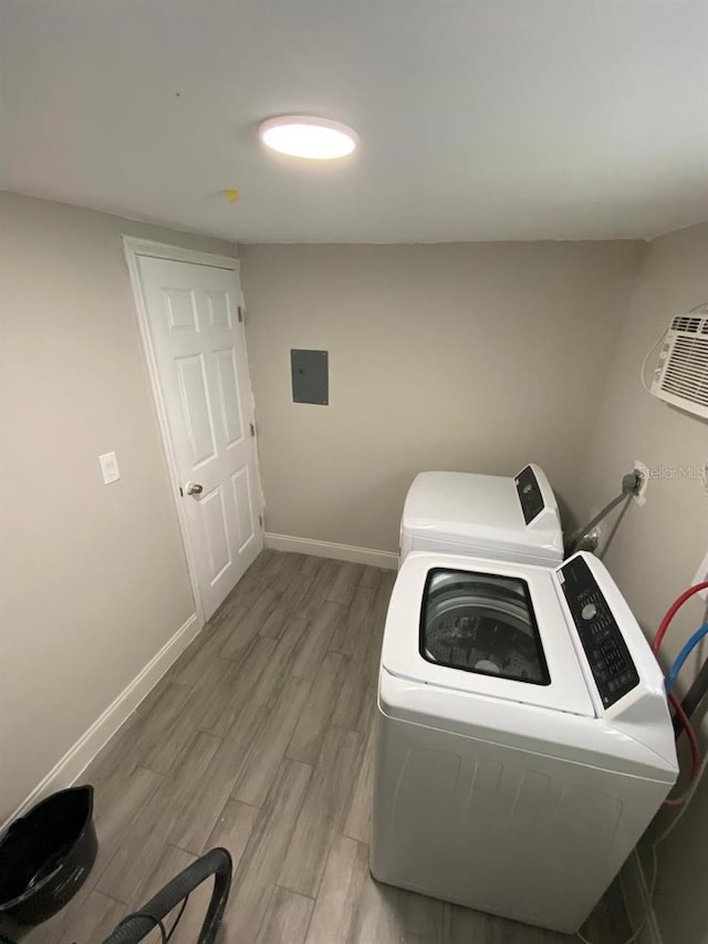 clothes washing area with electric panel, light wood-type flooring, and washer and clothes dryer