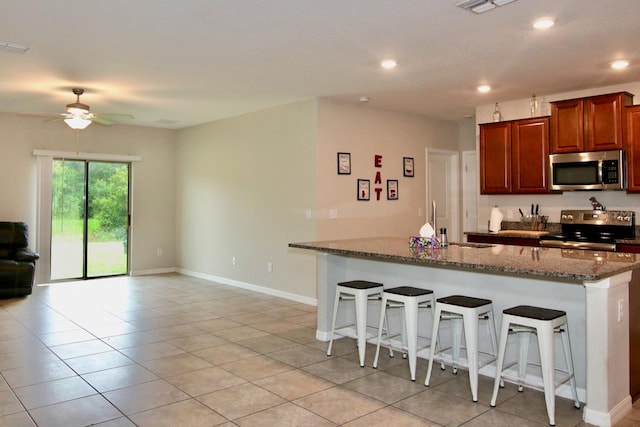 kitchen featuring a kitchen bar, stone counters, light tile patterned flooring, and appliances with stainless steel finishes