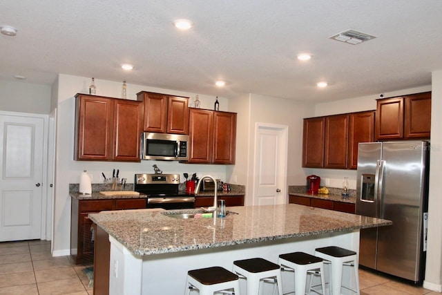 kitchen with sink, a kitchen breakfast bar, an island with sink, light tile patterned floors, and appliances with stainless steel finishes