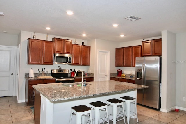 kitchen featuring sink, light tile patterned floors, an island with sink, appliances with stainless steel finishes, and a kitchen bar