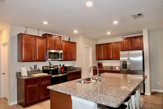 kitchen with appliances with stainless steel finishes, a breakfast bar, sink, light tile patterned floors, and a center island with sink