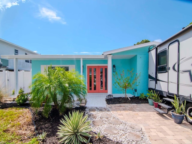 doorway to property with stucco siding, french doors, and fence