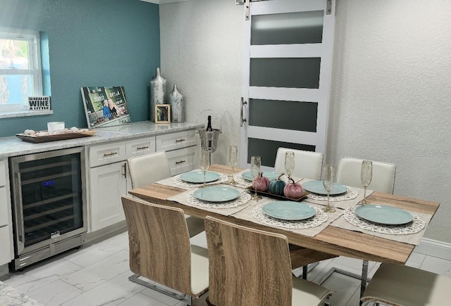 dining room featuring a textured wall, wine cooler, and marble finish floor