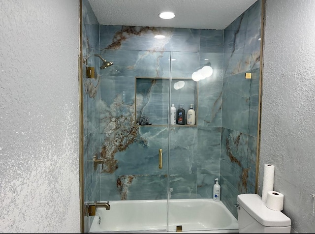 bathroom with a textured wall, bath / shower combo with glass door, and toilet