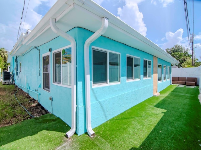 view of property exterior featuring fence, a lawn, central air condition unit, and stucco siding