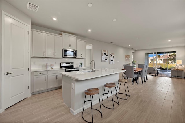 kitchen featuring sink, a breakfast bar area, appliances with stainless steel finishes, a kitchen island with sink, and backsplash