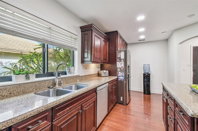 kitchen with light stone counters, stainless steel appliances, light hardwood / wood-style floors, and sink