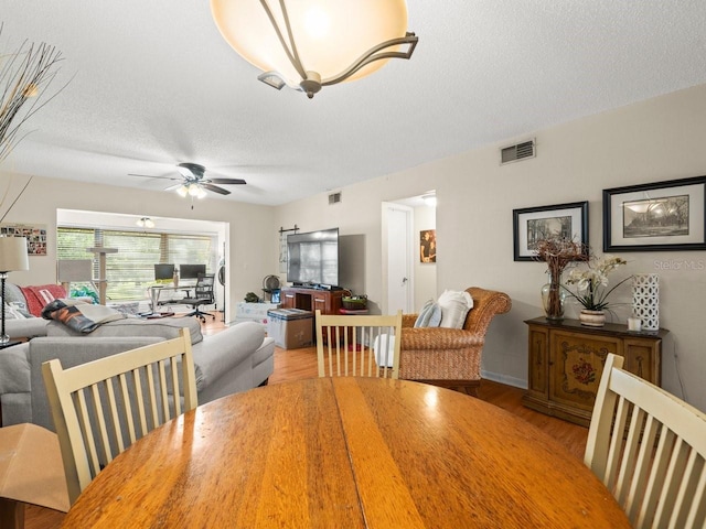 dining room with light wood-type flooring, ceiling fan, and a textured ceiling