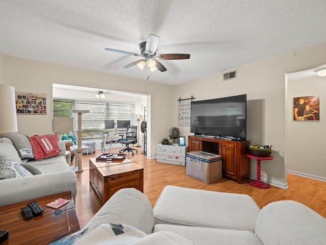 living room with ceiling fan, a textured ceiling, and light hardwood / wood-style floors