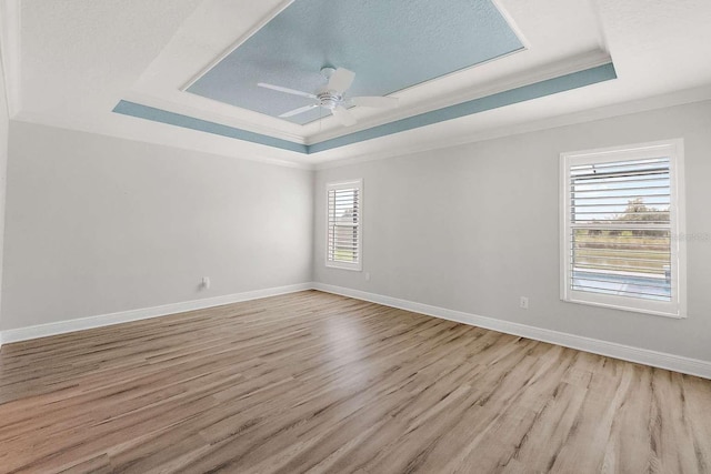 empty room featuring ornamental molding, a tray ceiling, light wood-type flooring, and a healthy amount of sunlight