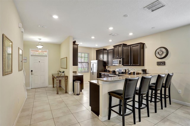 kitchen featuring kitchen peninsula, appliances with stainless steel finishes, a kitchen bar, and light tile patterned floors