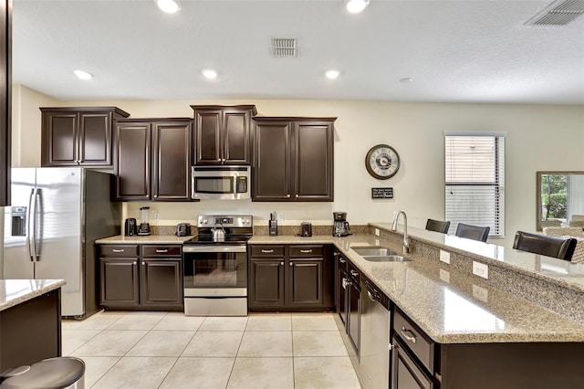 kitchen featuring sink, stainless steel appliances, a kitchen breakfast bar, light stone counters, and kitchen peninsula