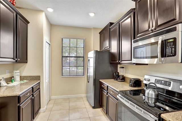 kitchen with a textured ceiling, dark brown cabinets, light tile patterned floors, and stainless steel appliances