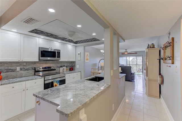 kitchen featuring white cabinets, ceiling fan, appliances with stainless steel finishes, backsplash, and light stone counters