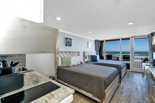 bedroom featuring access to exterior, sink, hardwood / wood-style floors, a water view, and floor to ceiling windows