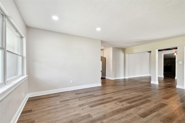 unfurnished room with a textured ceiling, plenty of natural light, and dark wood-type flooring