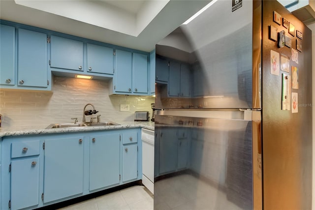 kitchen featuring blue cabinets, light tile patterned floors, sink, backsplash, and stainless steel refrigerator