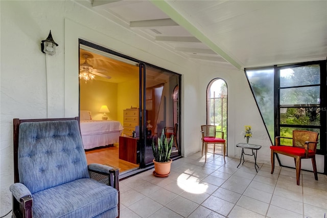 sitting room with ceiling fan, beamed ceiling, light tile patterned floors, and a healthy amount of sunlight