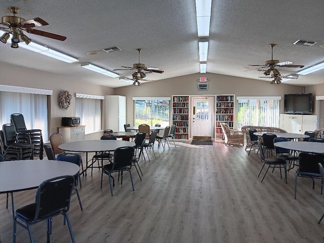 dining space featuring hardwood / wood-style floors, a healthy amount of sunlight, a textured ceiling, and vaulted ceiling