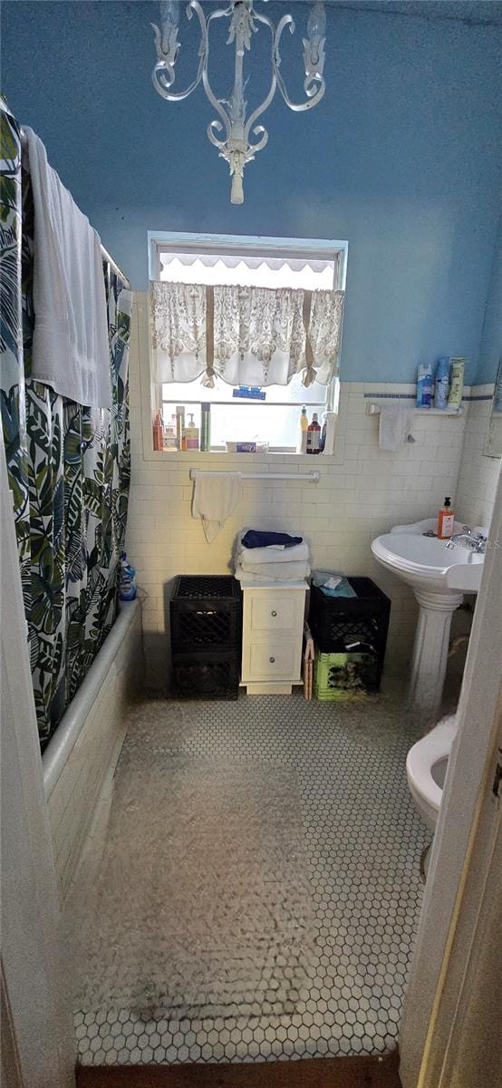 bathroom featuring a chandelier, tile walls, toilet, shower / tub combo with curtain, and tile patterned floors