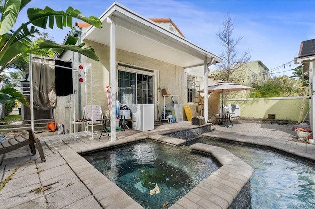 rear view of property with a swimming pool with hot tub and a patio area