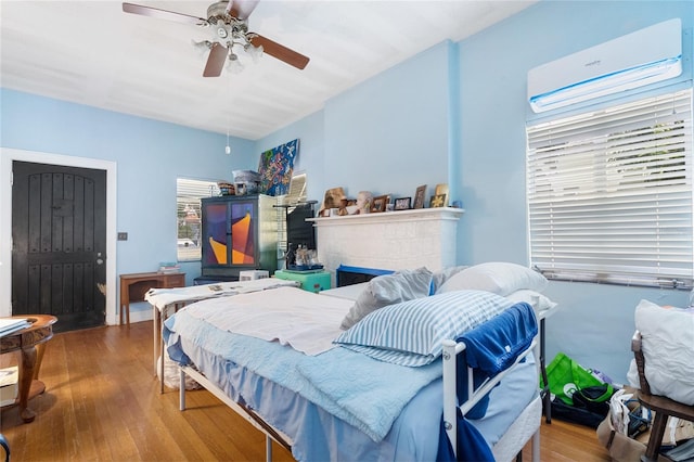 bedroom with a wall mounted AC, hardwood / wood-style flooring, a tiled fireplace, and ceiling fan