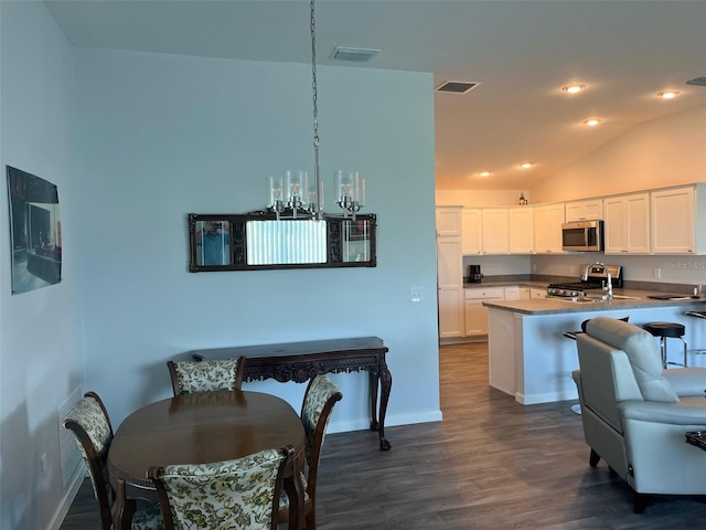kitchen with stainless steel appliances, vaulted ceiling, dark wood-type flooring, white cabinetry, and hanging light fixtures