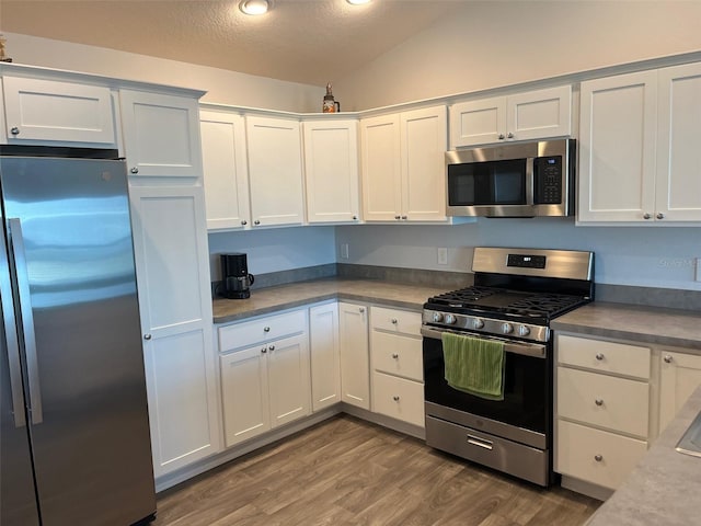 kitchen with stainless steel appliances, wood-type flooring, a textured ceiling, lofted ceiling, and white cabinets