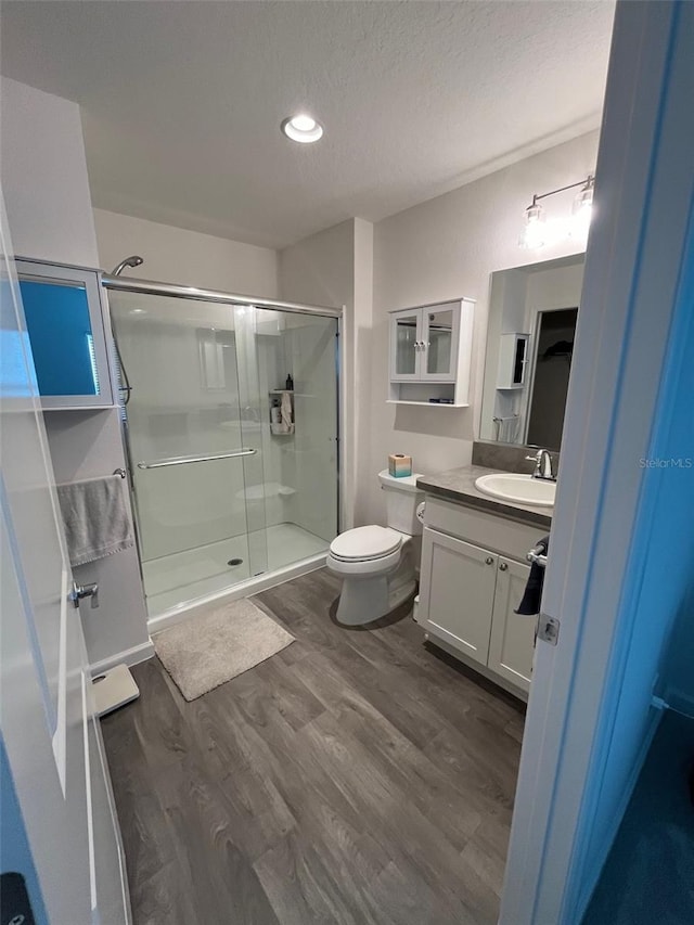 bathroom featuring walk in shower, vanity, a textured ceiling, wood-type flooring, and toilet