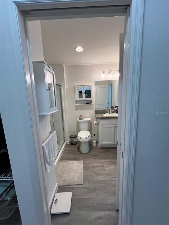 bathroom with hardwood / wood-style floors, vanity, toilet, and a shower with door