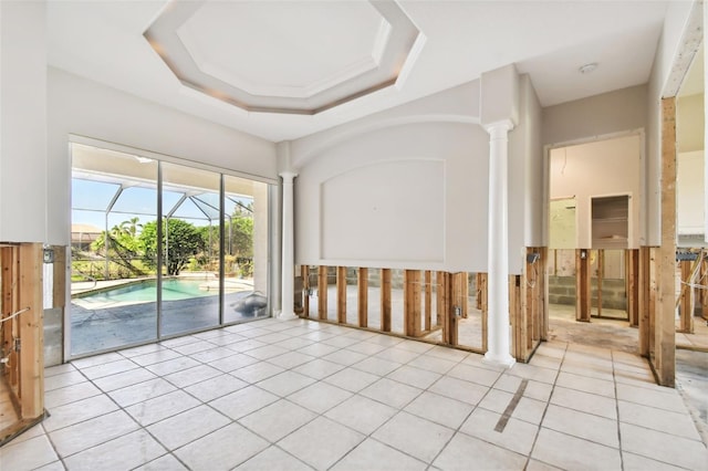 unfurnished room with light tile patterned flooring, a tray ceiling, and decorative columns