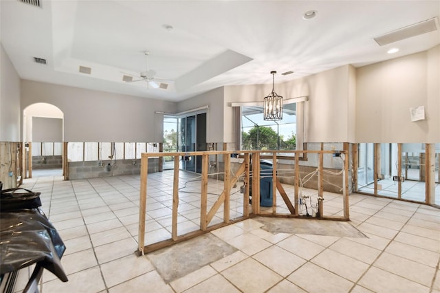 interior space with ceiling fan with notable chandelier, a tray ceiling, and light tile patterned floors