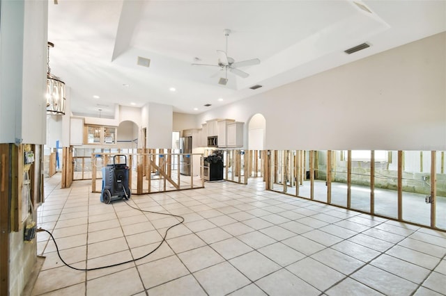 unfurnished living room with ceiling fan with notable chandelier, a tray ceiling, and light tile patterned floors