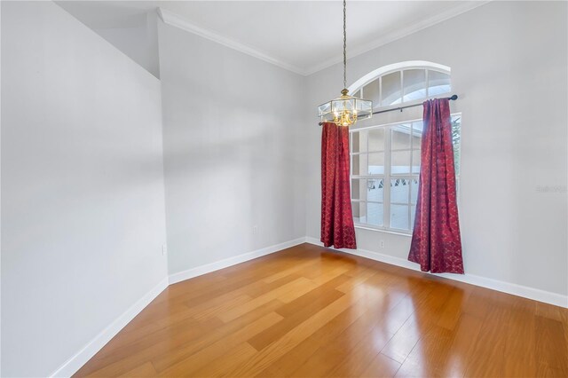 spare room with wood-type flooring, crown molding, and an inviting chandelier