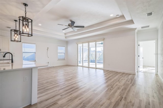 unfurnished living room featuring light wood-type flooring, plenty of natural light, sink, and a raised ceiling