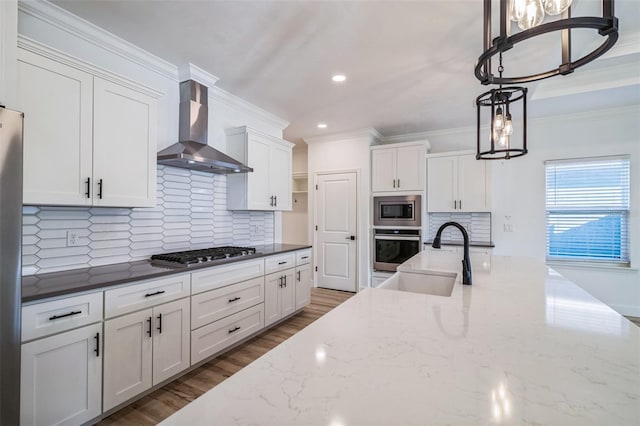 kitchen featuring hanging light fixtures, sink, wall chimney range hood, white cabinetry, and appliances with stainless steel finishes