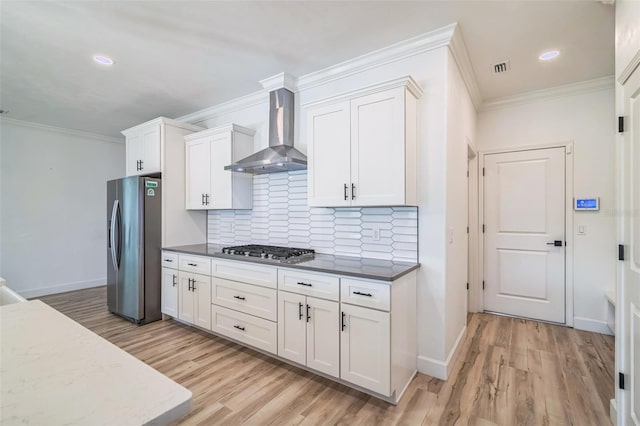 kitchen featuring white cabinets, tasteful backsplash, wall chimney exhaust hood, light hardwood / wood-style flooring, and stainless steel appliances